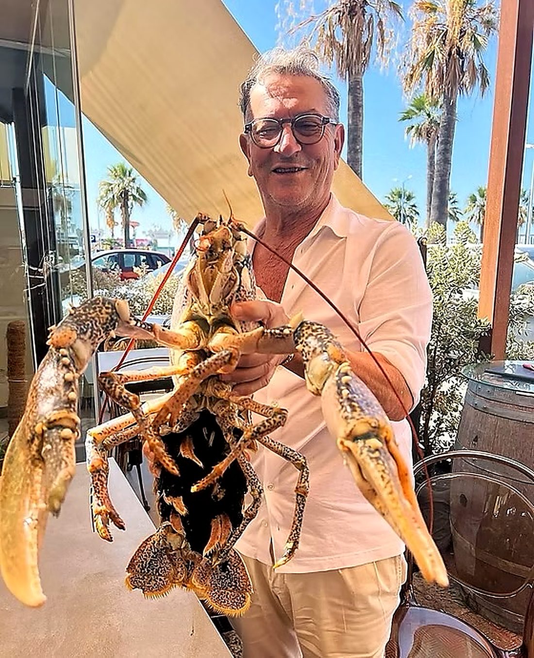 Il pescatore mostra con orgoglio un'aragosta viva appena scelta, con il lungomare di San Leone sullo sfondo
