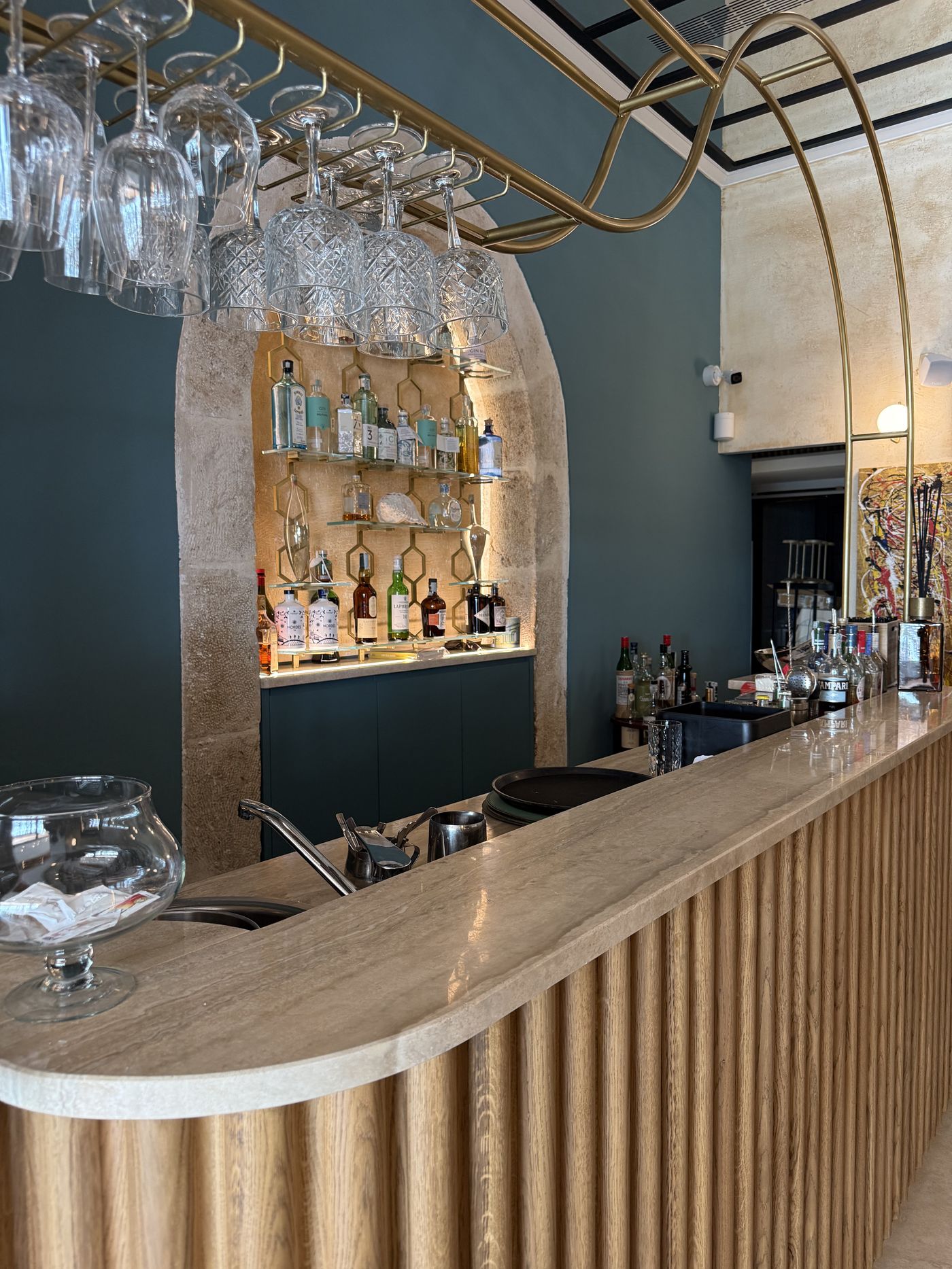Il bancone del bar sotto un arco in pietra locale, con calici sospesi e bottiglie in una nicchia illuminata