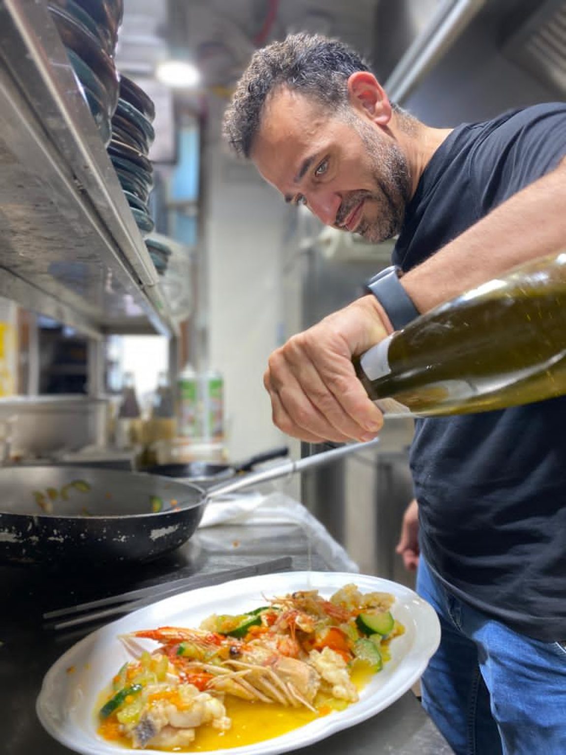 Lo chef rifinisce con un filo d'olio un piatto di scampi e verdure croccanti in cucina