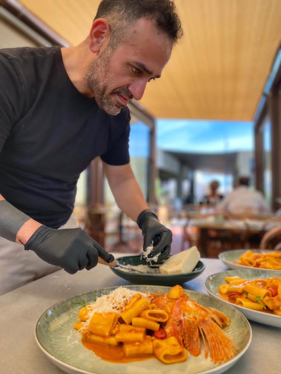 Lo chef manteca in terrazza un piatto di paccheri con scampi e gambero rosso