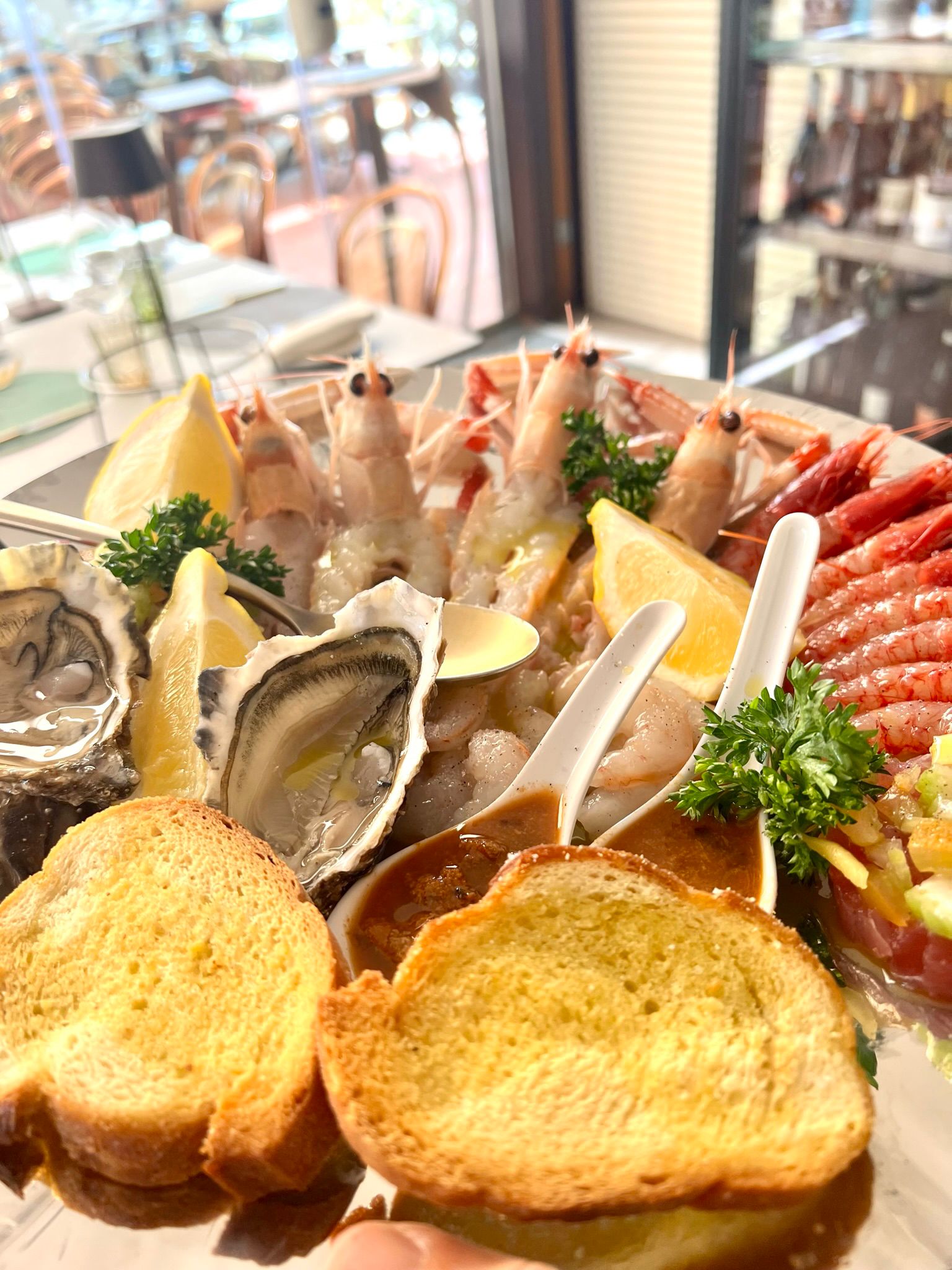 Tavolo apparecchiato con ostriche, gamberi, crostini e limone, affacciato sul lungomare